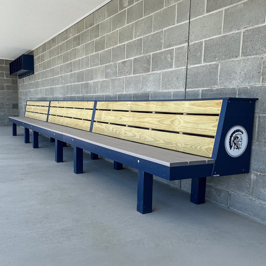 The Falcon Dugout Bench | MLB-Style 2-Tier Wood Baseball & Softball Bench features a wooden and blue metal design with a Spartan helmet logo, perfect for outdoor team areas or dugouts against concrete block walls.