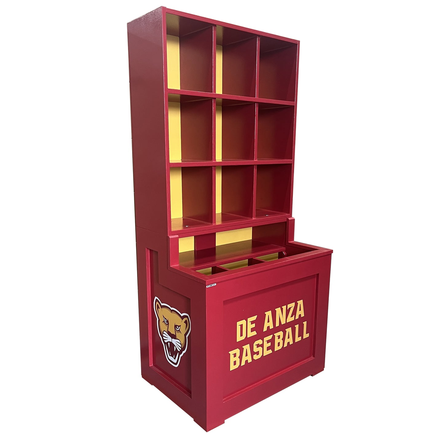 The Trooper Dugout Helmet and Bat Rack is a red shelving unit with yellow accents, featuring open cubbies and a lower storage compartment. A cougar mascot and DE ANZA BASEBALL in yellow are displayed on the front. Holds 9 helmets.