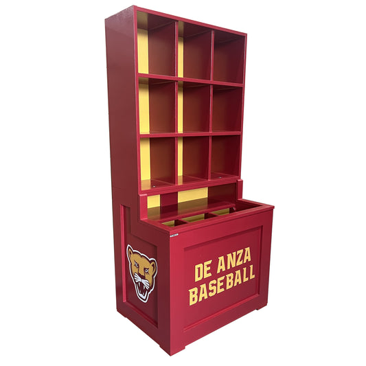 The Trooper Dugout Helmet and Bat Rack is a red shelving unit with yellow accents, featuring open cubbies and a lower storage compartment. A cougar mascot and DE ANZA BASEBALL in yellow are displayed on the front. Holds 9 helmets.