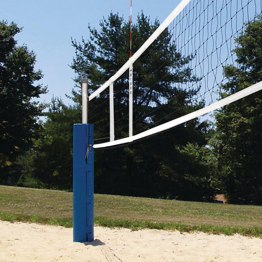 A Sand Volleyball Net stretches 28 feet between blue poles on a sand court, surrounded by grass and trees beneath a clear sky.