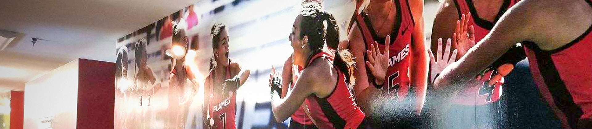 A wall mural showing female basketball players in red uniforms celebrating, giving high-fives, and smiling during a game.