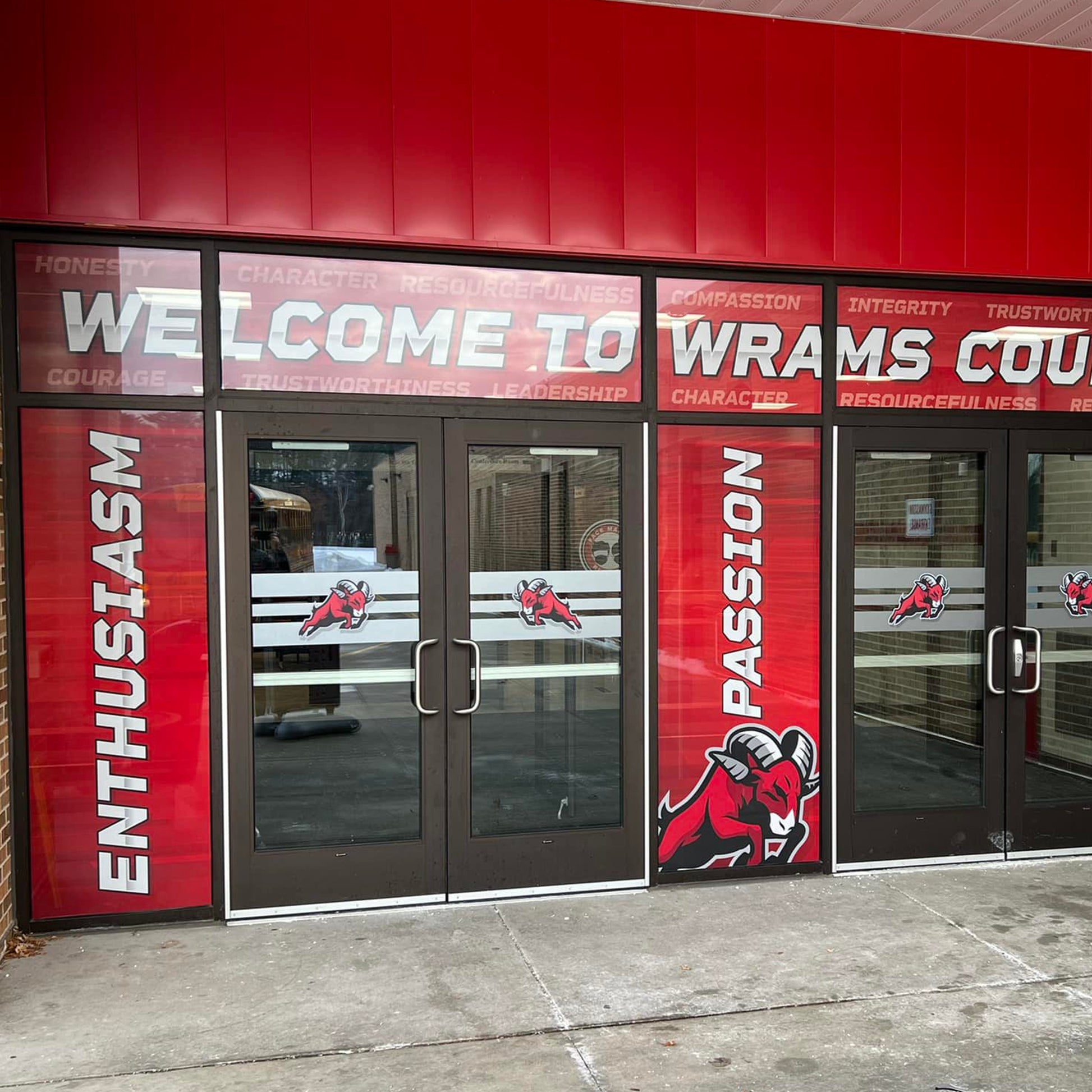 Perforated Window Film on entry doors with red banners and ram logos, plus WELCOME TO RAMS COUNTRY and values like honesty and integrity, provides unique branding while maintaining privacy.