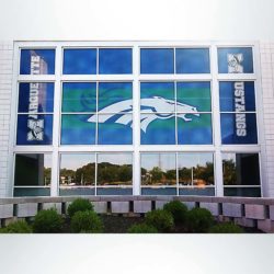 Window perf/see through film with blue, green and white graphics on windows at front entrance of school after branding.