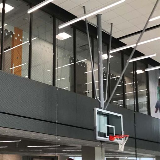 Ceiling mount basketball hoop in the down position. Hanging in front of a gray wall with windows above it.