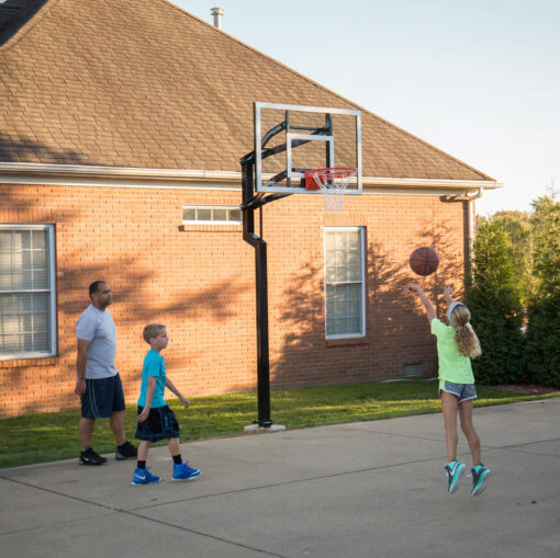 People playing on a Goalsetter Contender 54 in-ground basketball hoop in a backyard