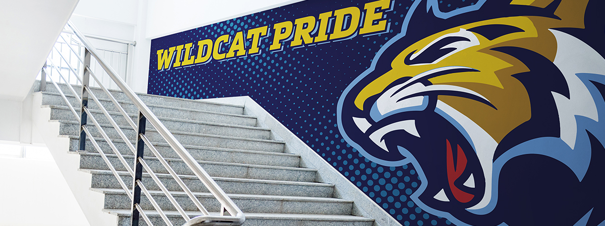 Blue vinyl wrap with Wildcat Pride in yellow text and a yellow wildcat with white stairs in front of the wall.