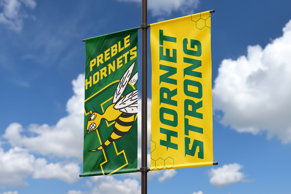 Two green and gold banners with the words preble hornets on one and a hornet and hornets strong on another, both attached to a black pole.