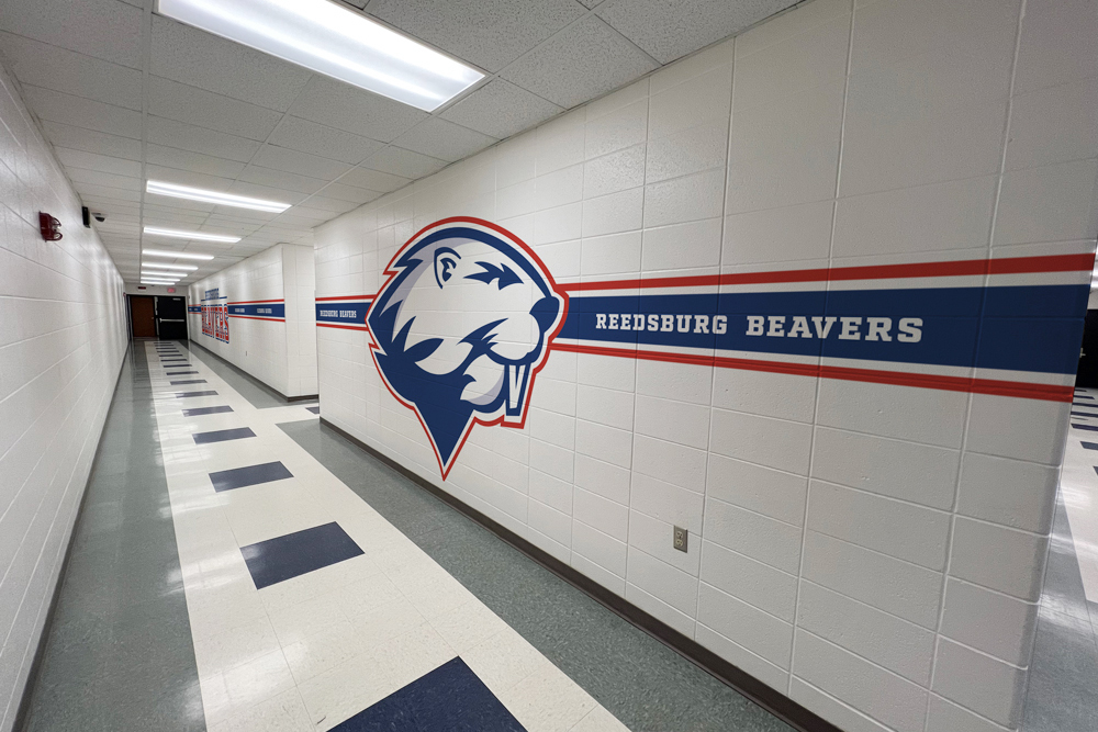 White cement block wall with horizontal bliue and red vinyl banding graphic with a beaver in the middle in school hallway.